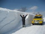 大人の男性の高さまで積もった雪の横に立つ男性の写真