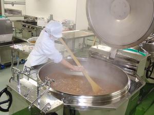 給食センターで調理員が大きなしゃもじで鍋をかき混ぜている写真