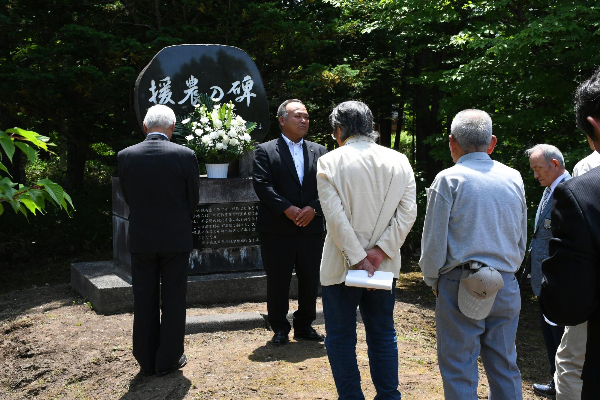碑の前で挨拶をする世話人の高橋正秀さん