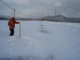 スノーポールを持ち道路横に立っている人の写真