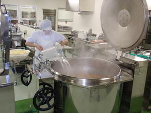 給食センターで調理員が大きな鍋に水を注いでいる写真